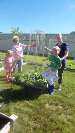 Garden club plants, weeds, and harvests to feed the hungry Sue Daley joins Mignon Teeple and her children Aubry and Nolan to plant a second crop of pole beans (Photo by Frances Ruth Harris)