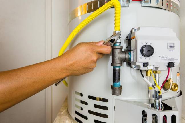 Water Heater Basics Plumber installing a gas line on a newly installed water heater tank. Great concept for plumbing, water heater repair, installation & maintenance for your next project.