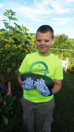 Aiden Fitzpatrick finds an overgrown zucchini under big leaves (Photo by Frances Ruth Harris)