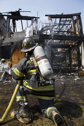A firefighter places water on the rear wall that is ready to collapse of a burned out townhouse (Photo by Robert Breese)