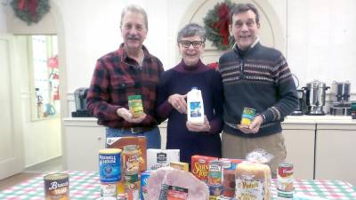 Food pantry volunteers Jim and Pat Snodgrass (left) and Bruce Baker with groceries that will help feed those in need at Christmas. Each family may chose between a turkey or a ham. The food pantry has found that the need for food has steadily increased over the past year.