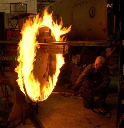 A preservation specialist ignites gas jets to create a ring of fire in order to expand a steel tire, prepping it for replacement (National Park Service photo)