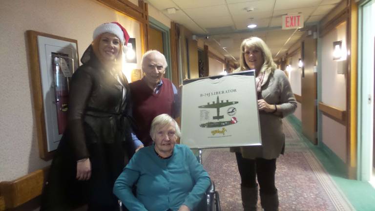 American Legion Auxiliary President Katie Jo Kardel stands next to veteran Ray Smith while Belle Reve’s care worker, Irina Abayeva, holds a framed tee shirt of Ray’s B-24. Ray’s wife, Alice, is seated. (Photo by Frances Ruth Harris)